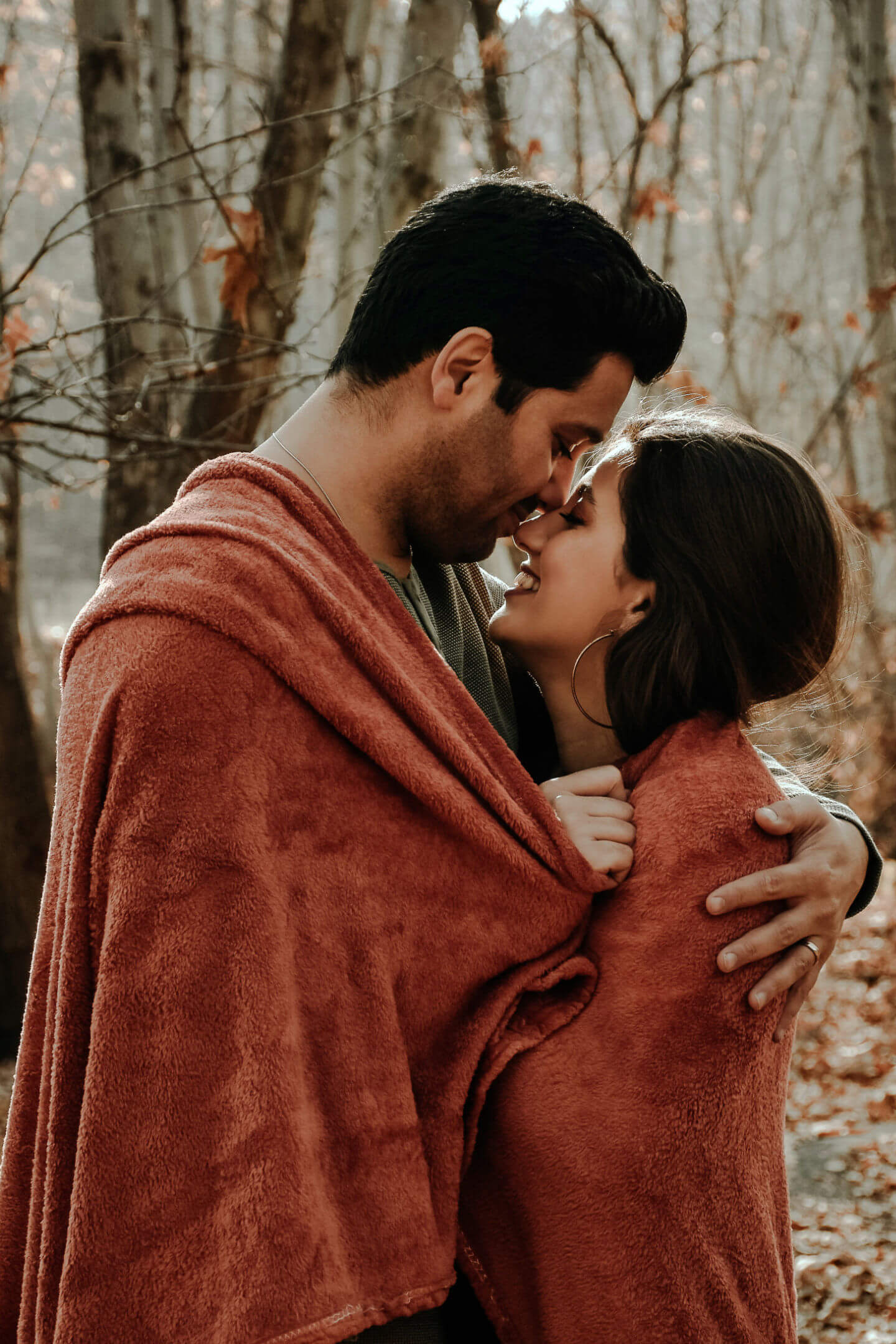 Man and woman embracing in the woods while wrapped in a blanket